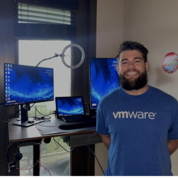 VMware - Man in a blue VMware t-shirt in front of his home office set up 