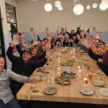 CrowdStreet, Inc - Large gathering of smiling CrowdStreet Builders at dinner with their hands raised in celebration.