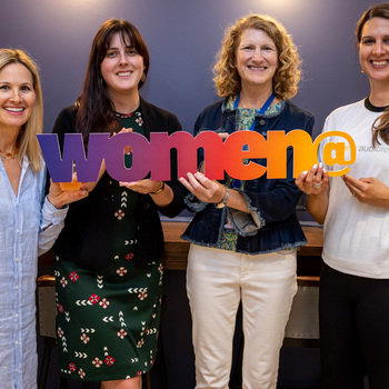 Audible - Four women smiling for a photo holding a "women@" sign